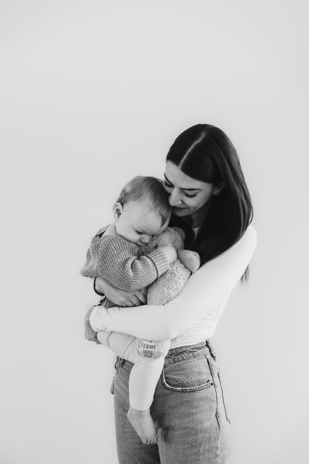 St. John's photographer captures a tender black and white portrait of a mother embracing her baby in a soft, minimalist setting.