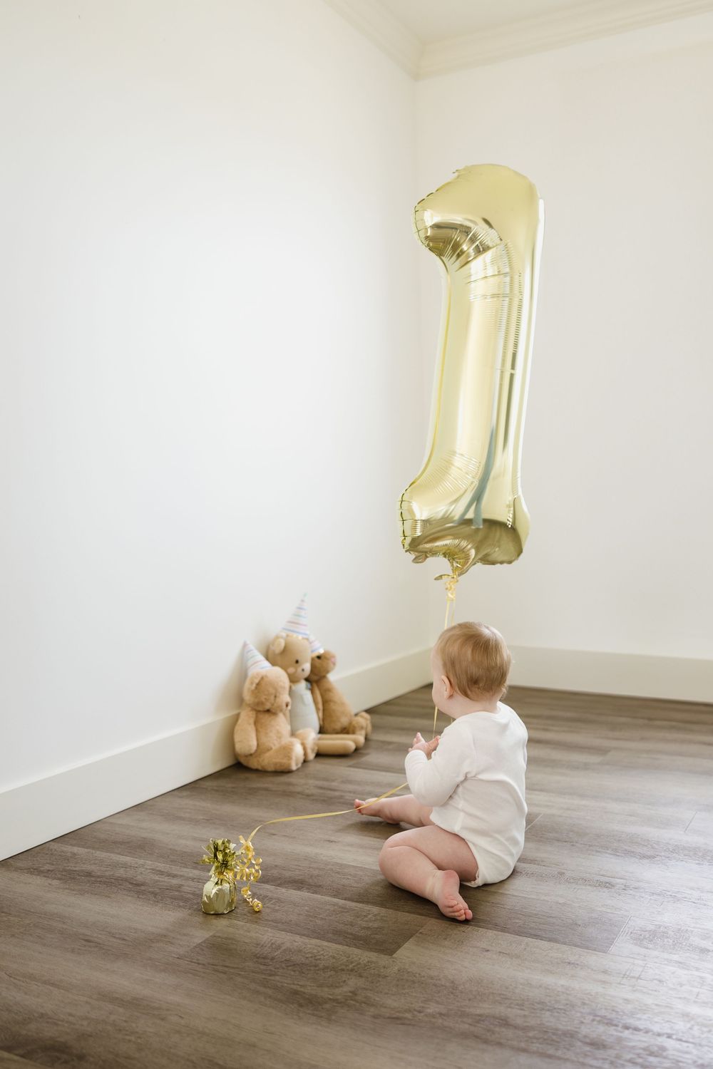 St. John's photographer captures baby sitting on floor with large gold number 1 balloon and stuffed animals for first birthday celebration.