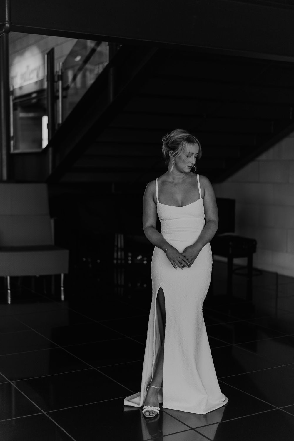 Newfoundland wedding photographer captures elegant woman in white fitted gown stands in dramatic black and white lighting.