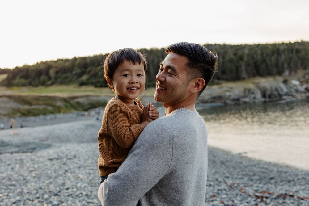 Parent and child sharing joyful laughter together on a rocky beach.