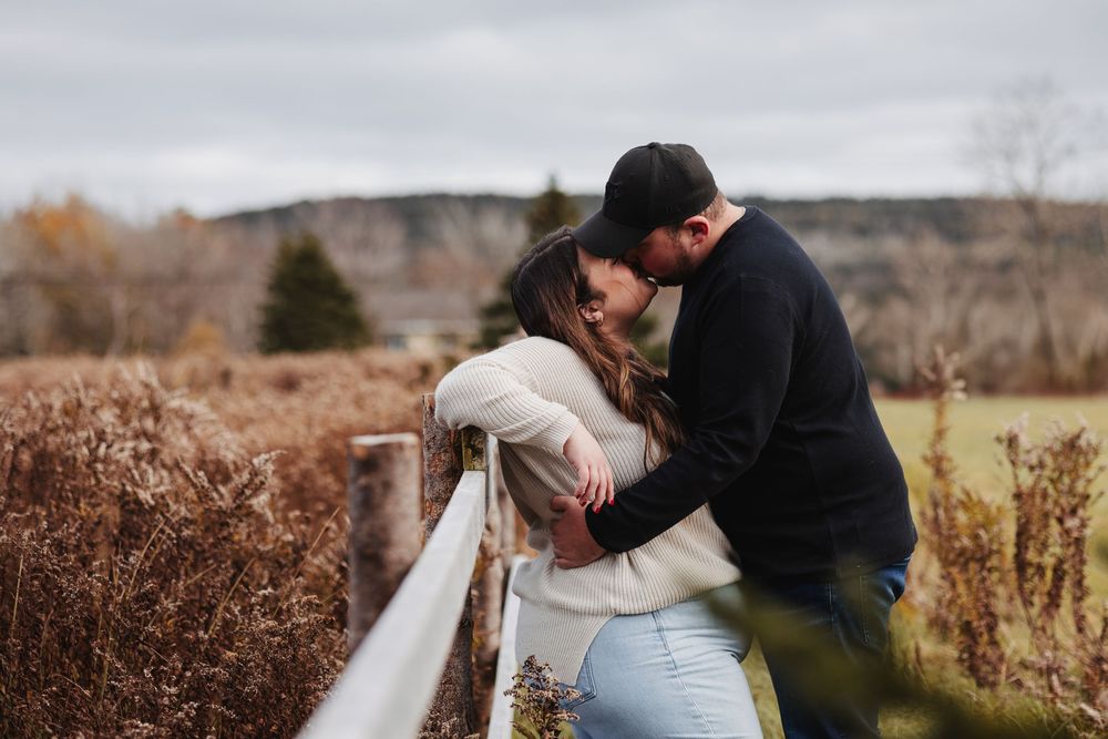 Romantic couple embracing by rustic fence in rural autumn landscape.