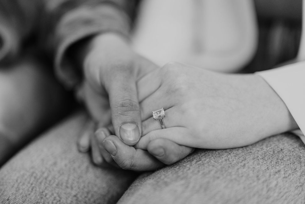 Close-up shot of hands gently holding an infant's small finger against a soft, monochromatic background.