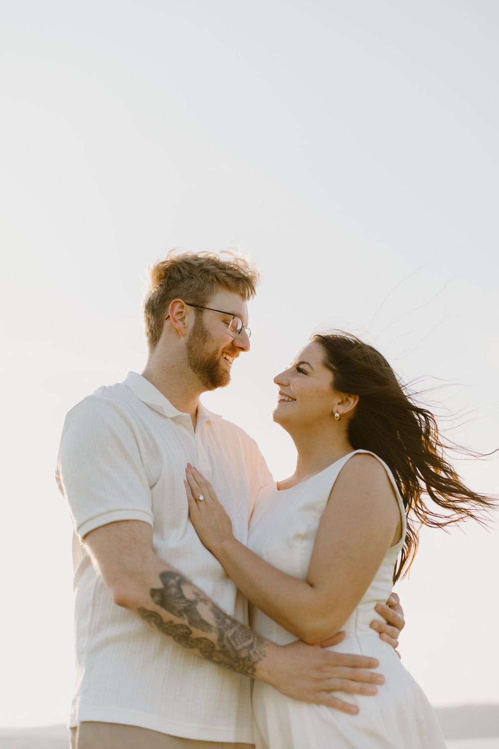 A couple in white clothing embraces and smiles at sunset creating a series of romantic silhouettes against the sky.