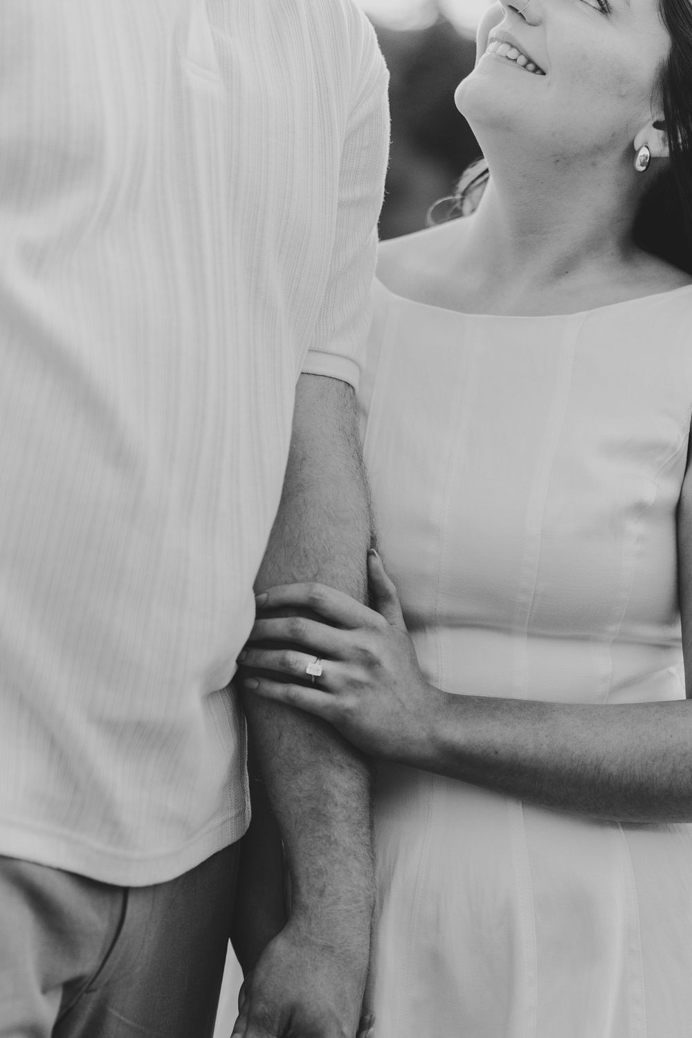 Black and white close-up photo showing intimate moment between couple in light colored clothing with hands touching.