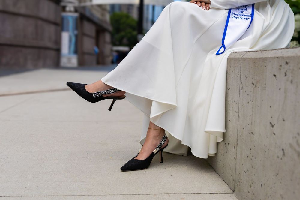 Woman in white flowy skirt seated outdoors, wearing elegant black slingback kitten heel pumps.