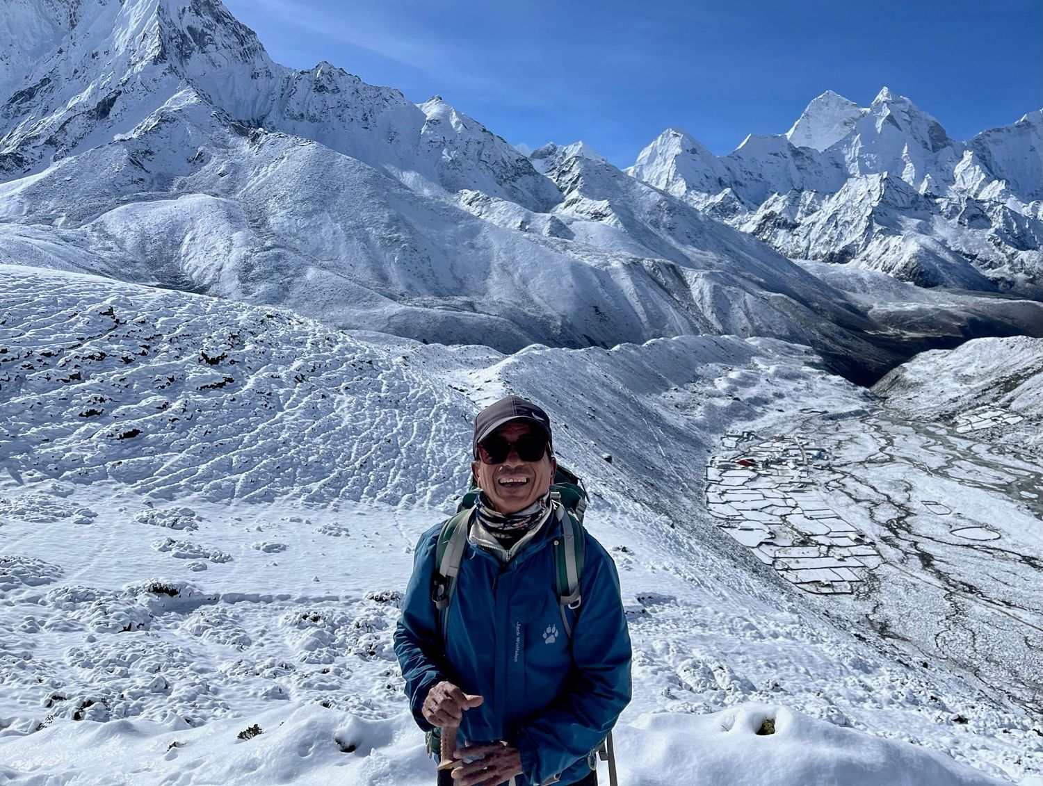 Snow-covered Himalayan mountain peaks under bright blue sky with climbers in distance.