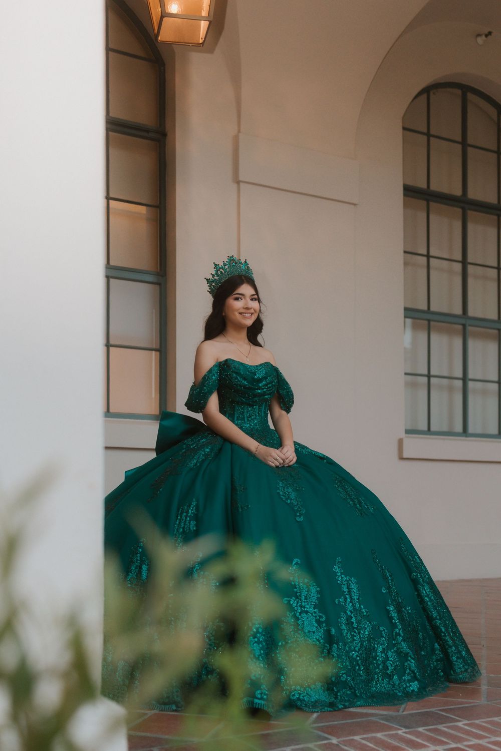 A green quinceanera dress with puffed sleeves and full skirt is showcased in an outdoor setting with pillars.