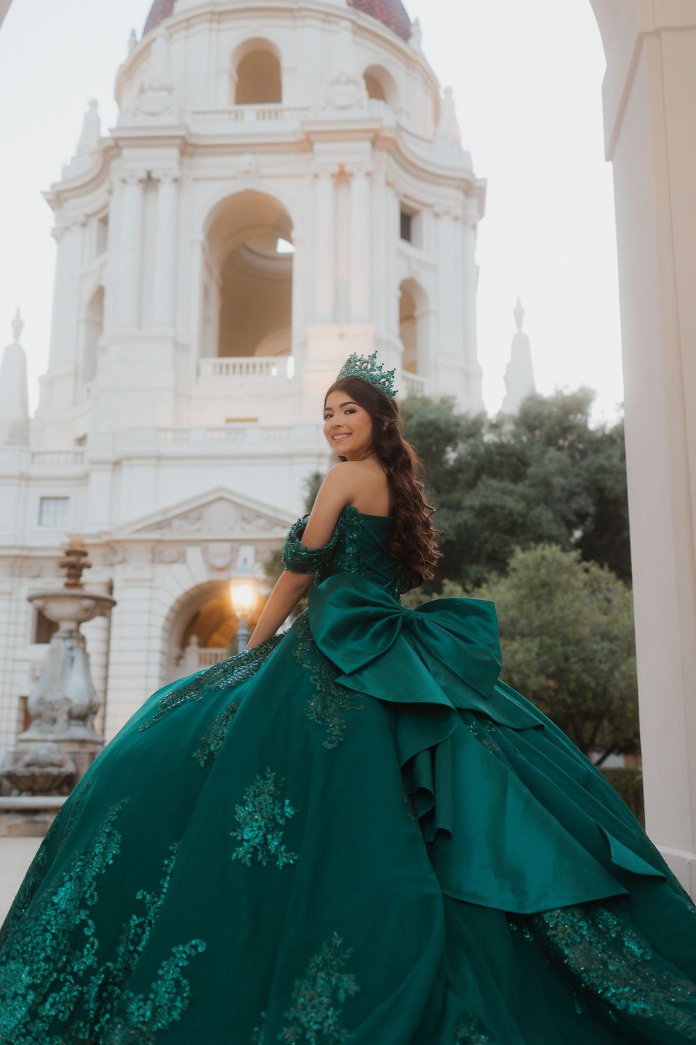 Elegant emerald green ball gown with lace details photographed in front of Pasadena City Hall's iconic bell tower.
