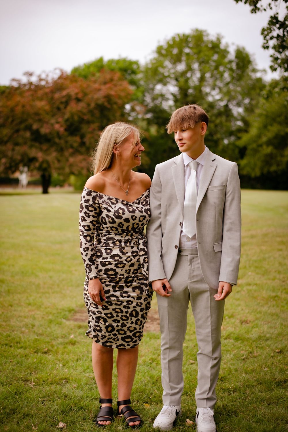 A couple dressed in formal attire pose together on a grassy lawn during a special occasion.