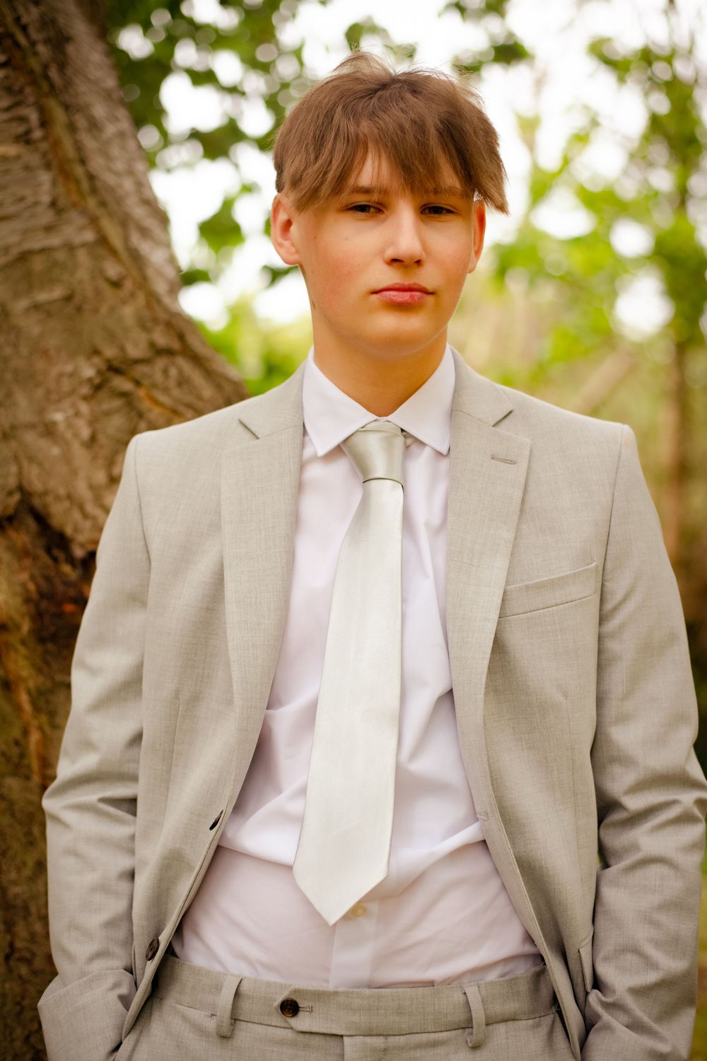 Professional portrait of a person in a light gray suit wearing a white shirt and tie standing by a tree.