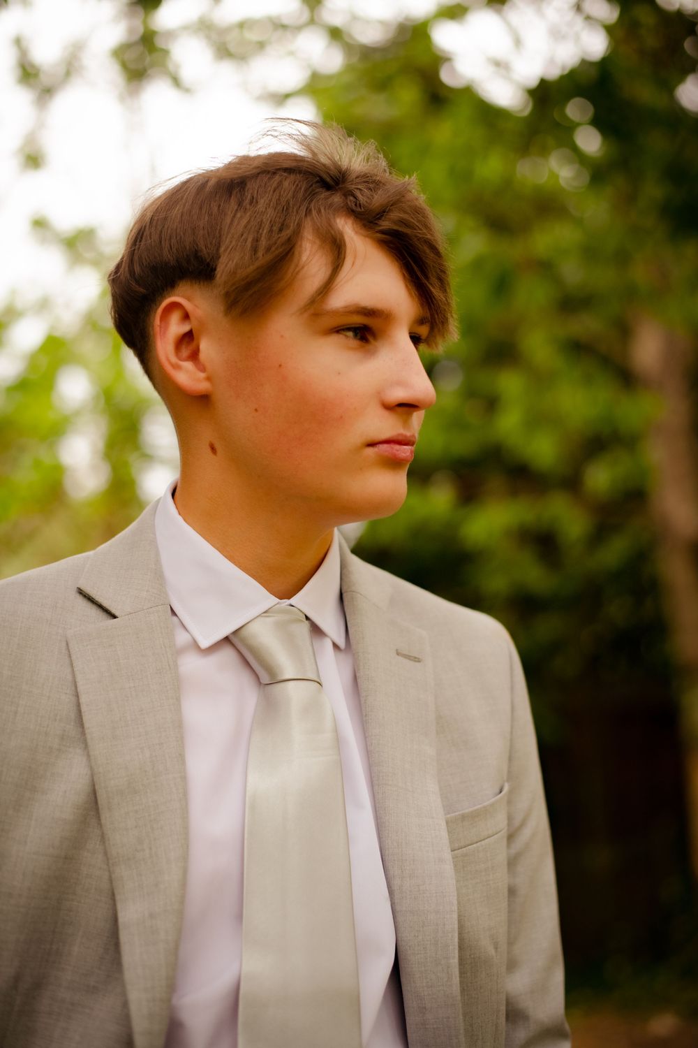 Side profile portrait showing a person in formal attire against a blurred green natural background.