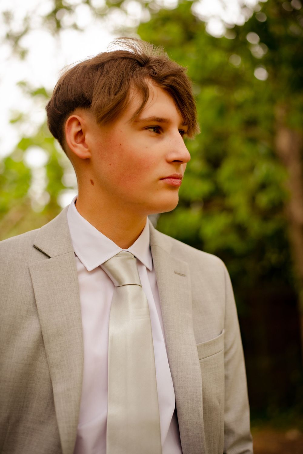 A portrait in a light gray suit and tie against a blurred green outdoor background.
