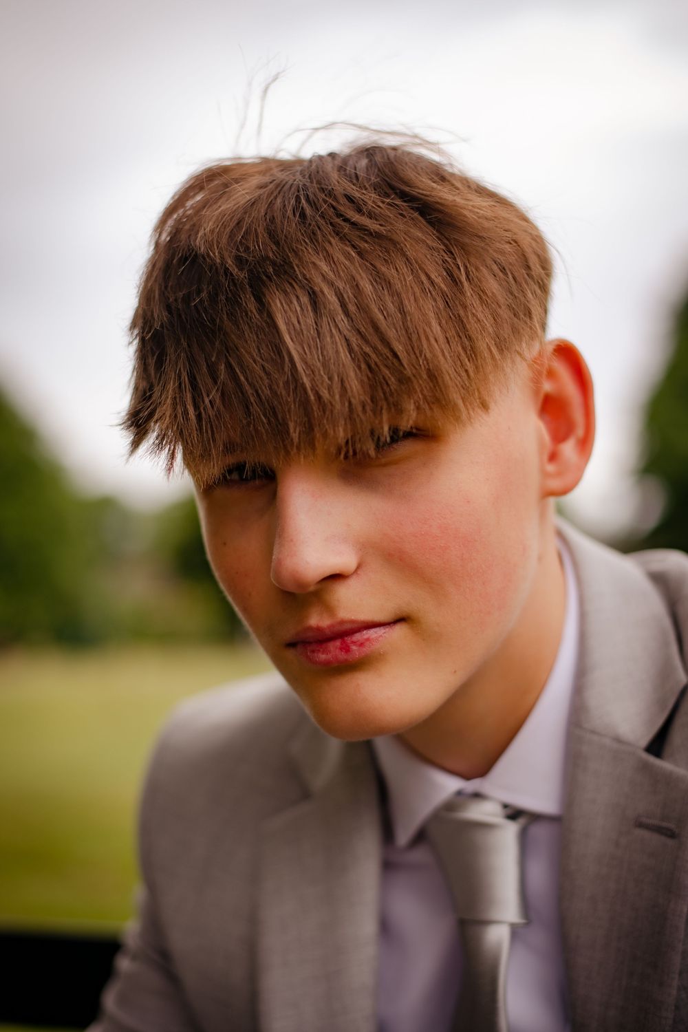 Close-up portrait of someone wearing a gray suit with tousled brown hair against a soft focus background.