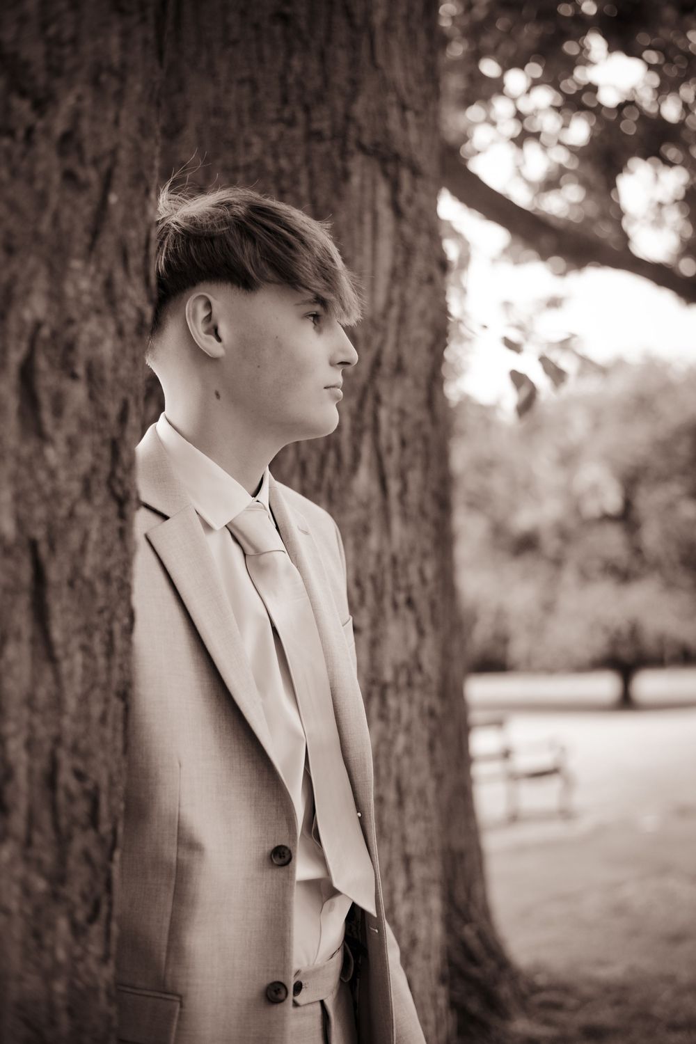 Sepia-toned side profile portrait against a tree trunk with soft natural lighting in the background.