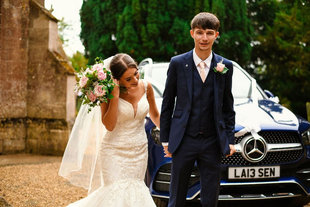 Wedding couple poses together outdoors near a classic Mercedes car on their special day.