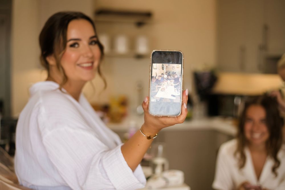 Someone in a white robe shows a photo on their phone while getting ready in a brightly lit room.