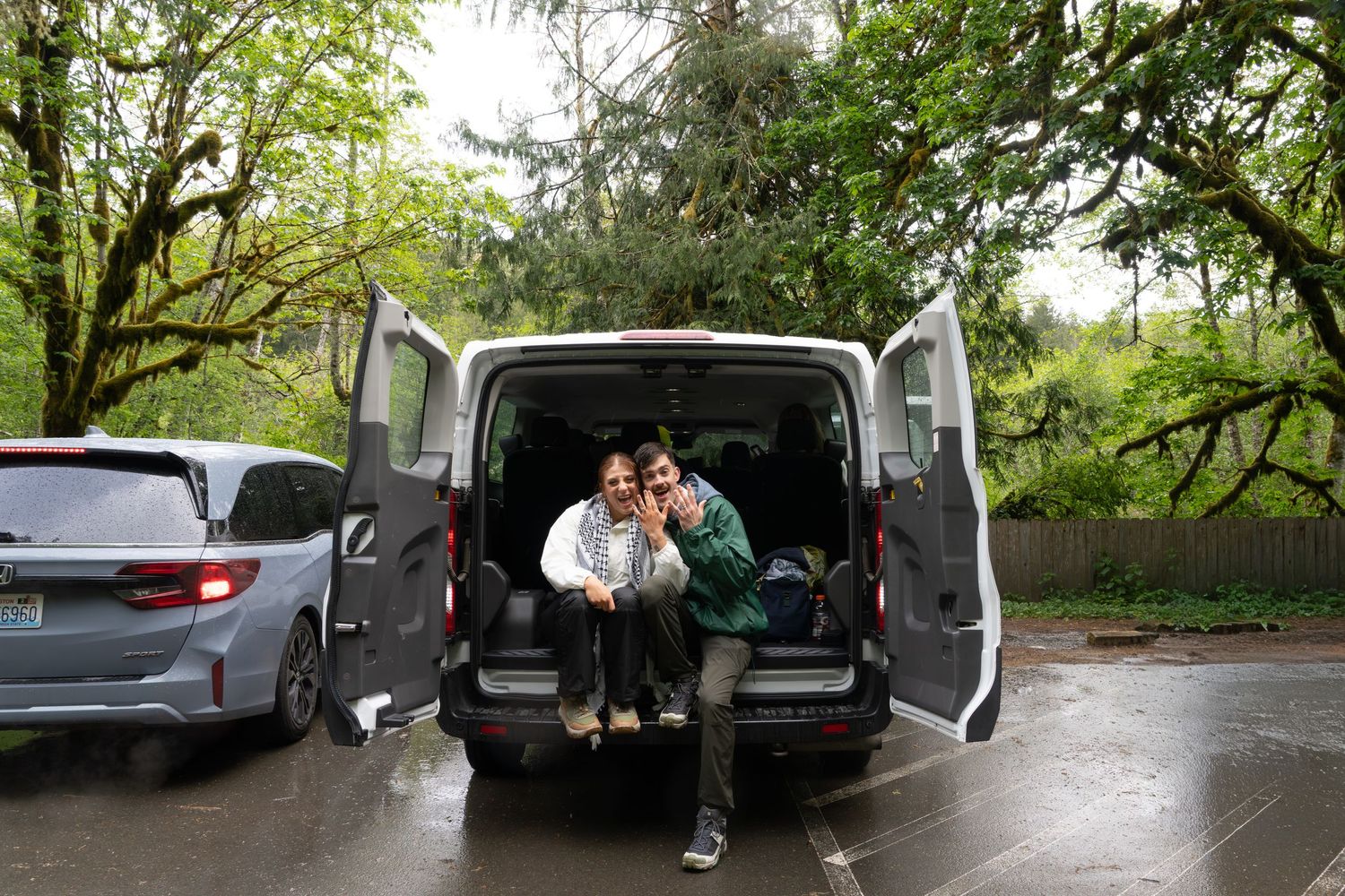 Two people sitting together in the open back of a van in a rainy parking lot in Olympic National Park, Captured by Savvy Photography