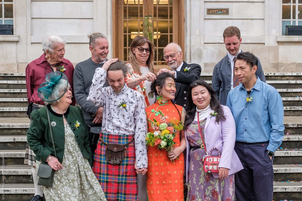 A cheerful group in festive attire stands together on stone steps outside a grand building after a special celebration.