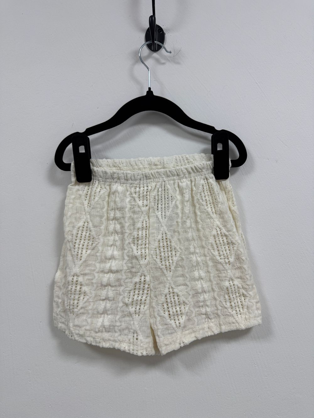 White lace shorts with delicate floral pattern displayed on hangers from multiple angles showing feminine details and texture.