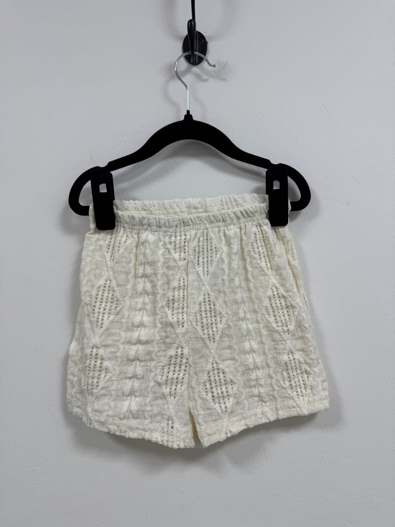 White lace shorts with delicate floral pattern displayed on hangers from multiple angles showing feminine details and texture.