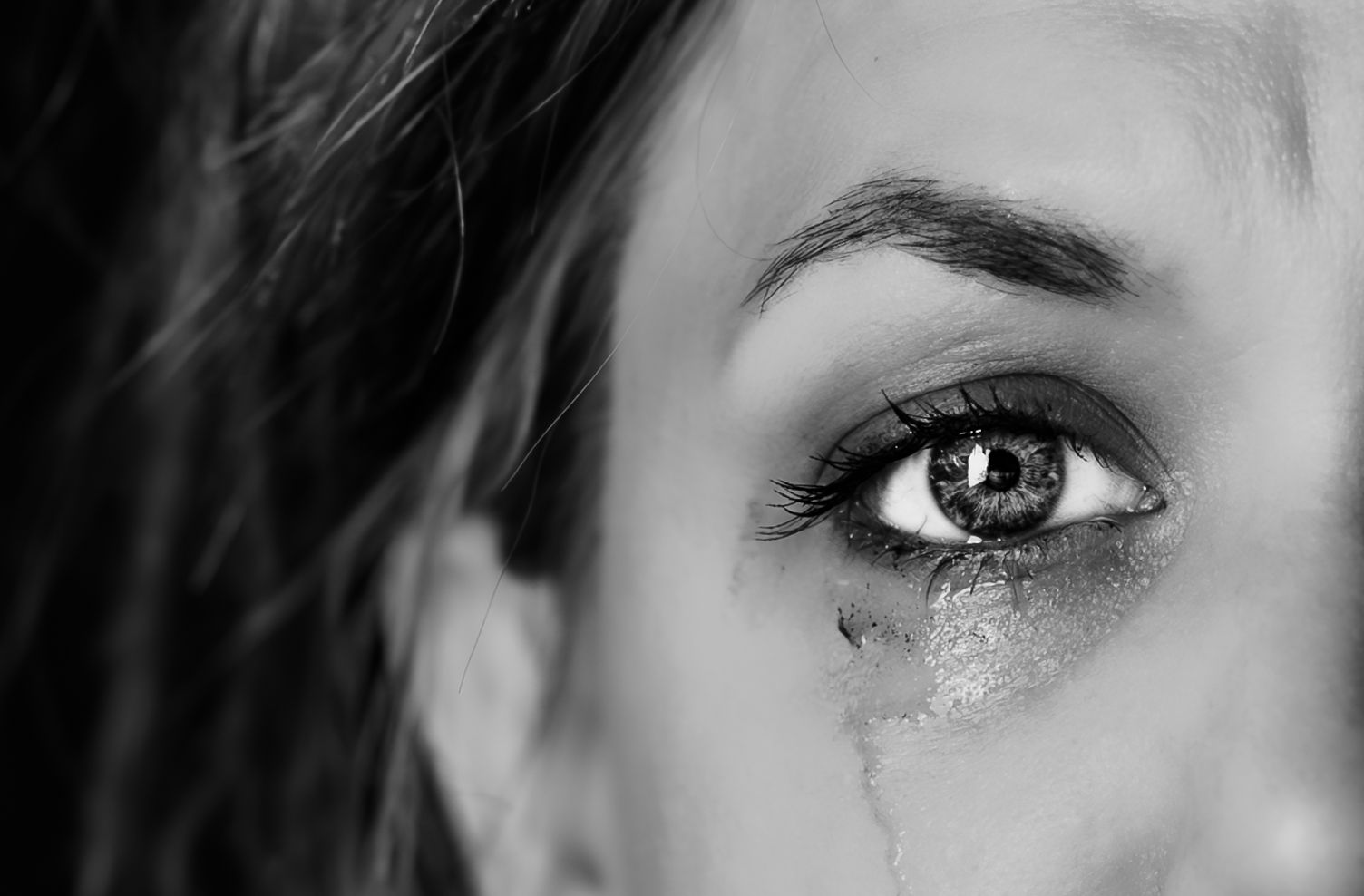 Black and white close-up photograph of a tearful eye with mascara running down the cheek.