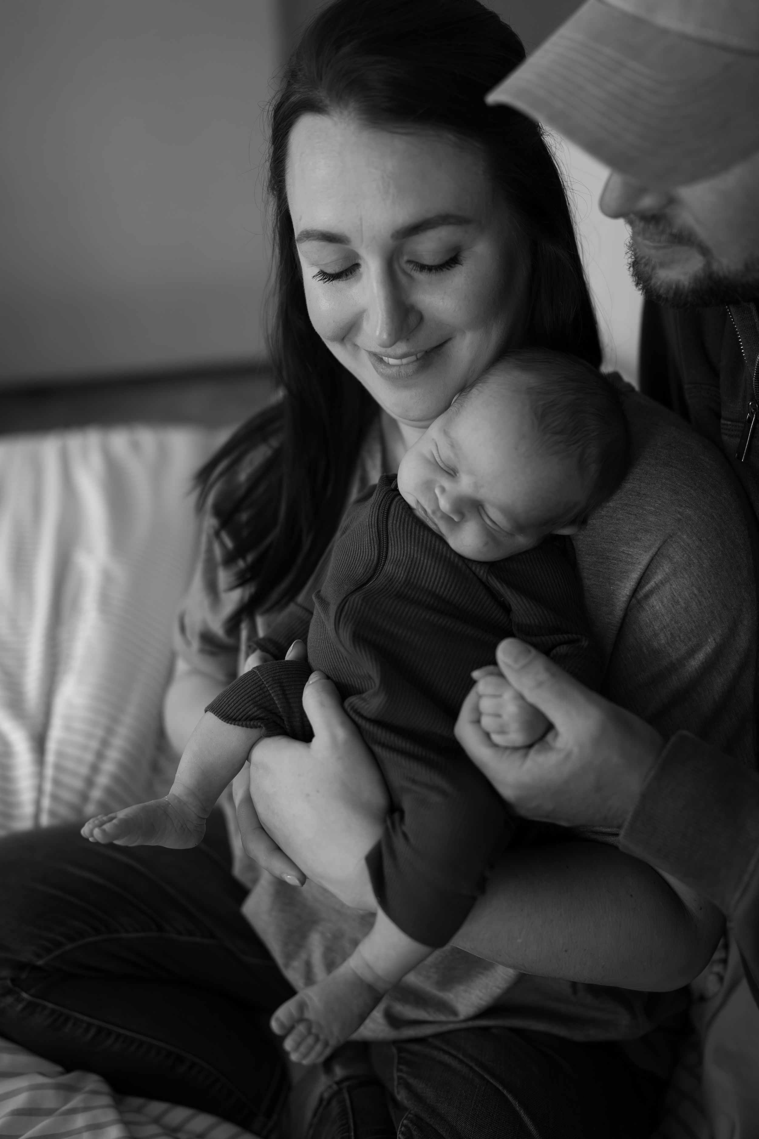 A tender black and white moment showing a family resting peacefully together with their baby on a couch.