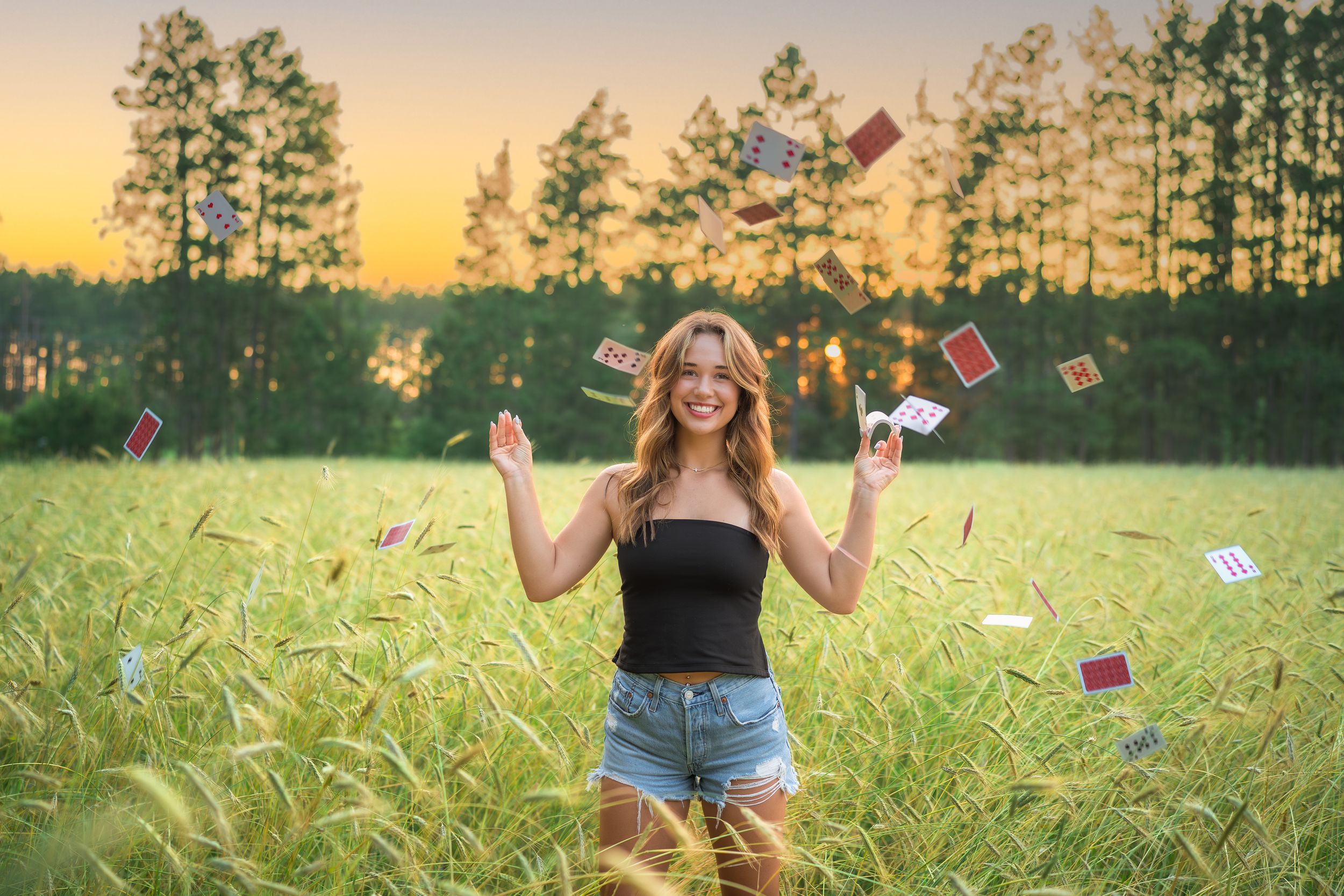 Playing cards scatter through tall grass in a golden sunset field with trees in the background.