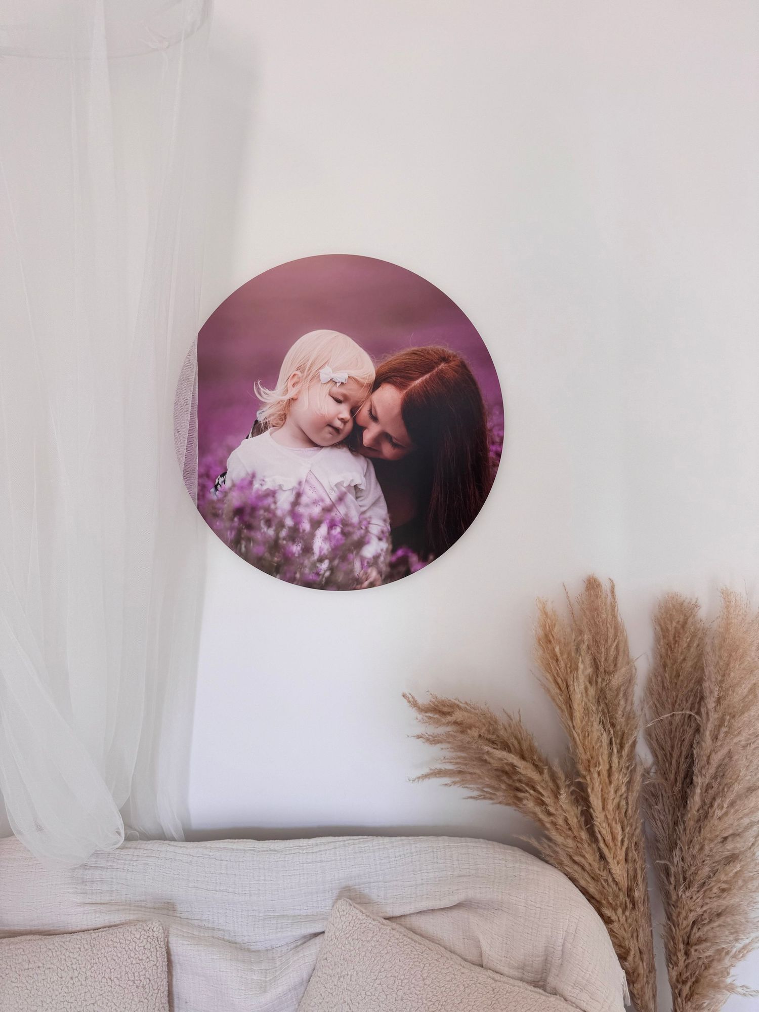 A circular photo on display against a white wall, with dried pampas grass stalks decorating the corner of the room.