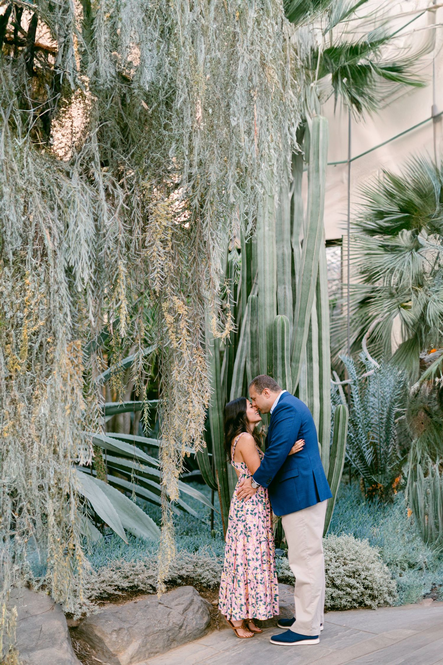 Two people share a romantic moment beneath cascading Spanish moss in a dreamy garden setting.