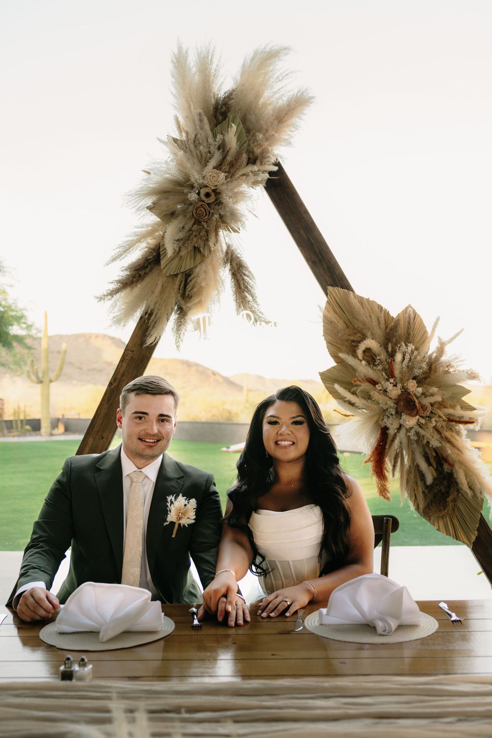 A couple sharing joyful moments at their wedding reception with dried palm decorations.