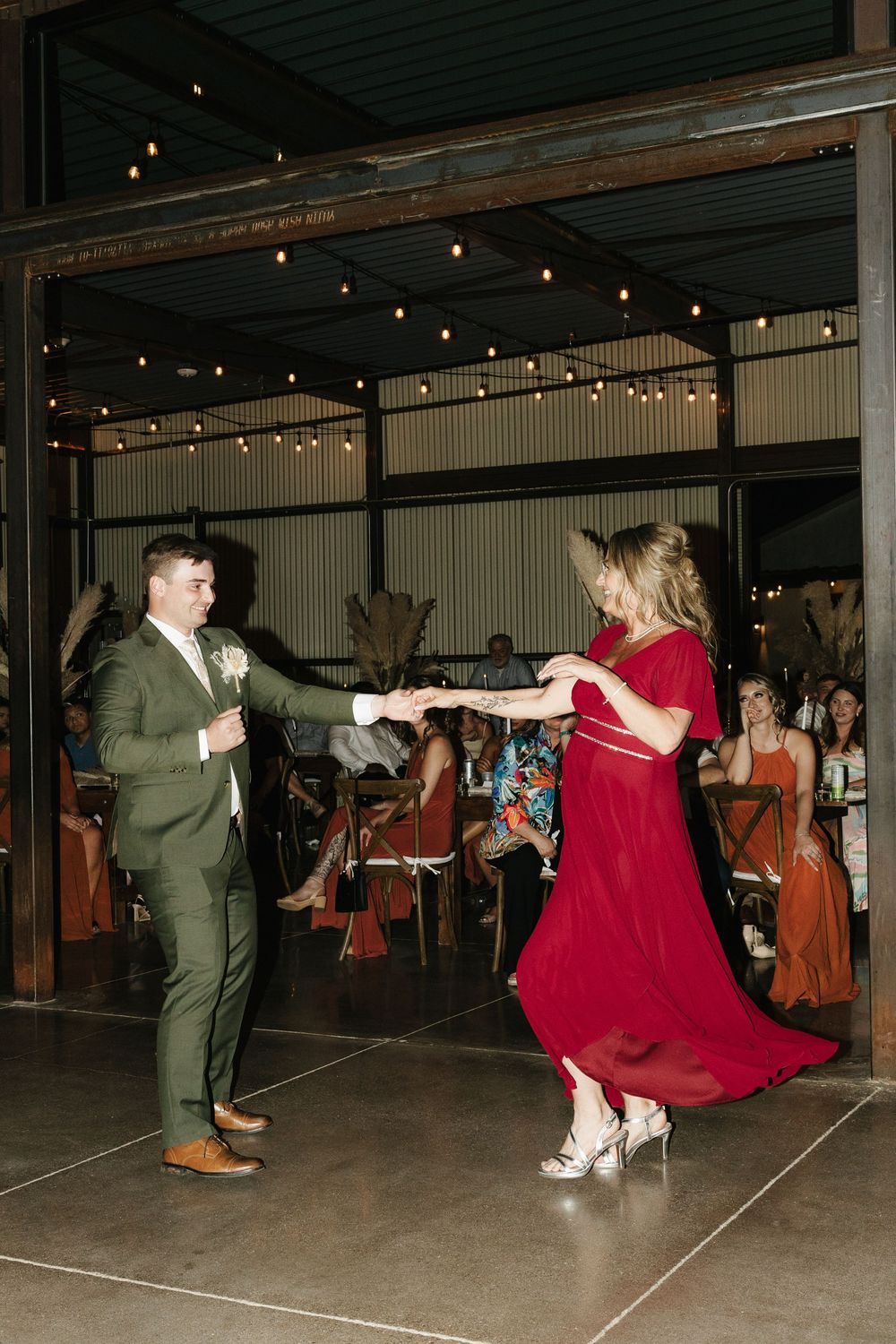 Wedding guests dancing energetically in formal attire under string lights.