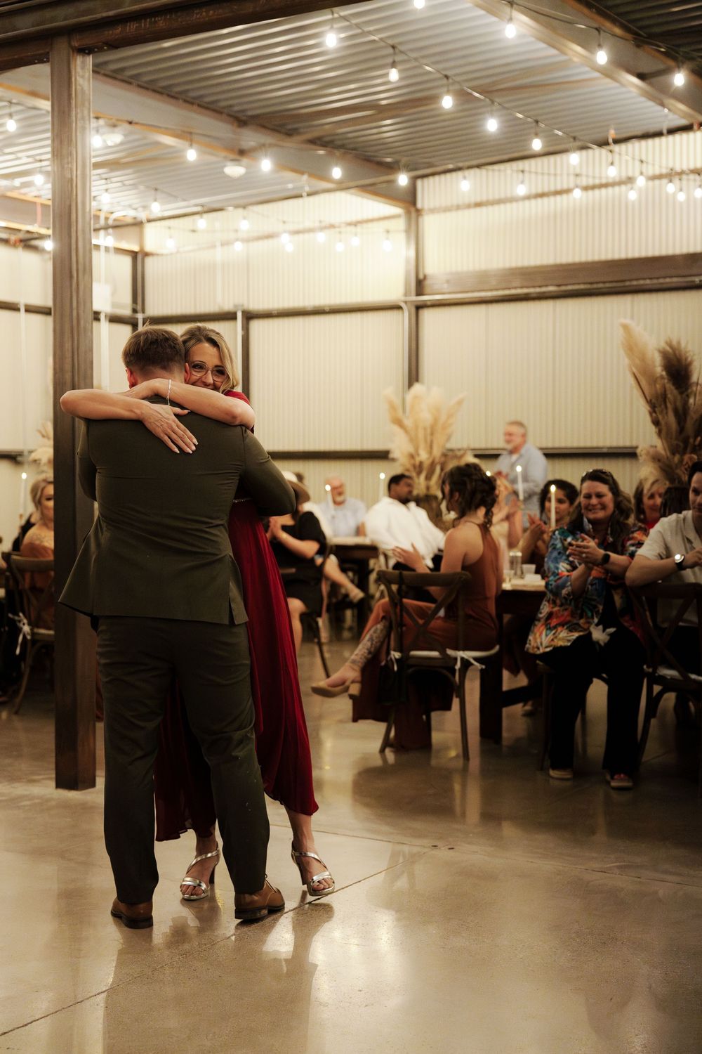 Wedding guests dancing together at a reception in an industrial-style venue with string lights overhead.