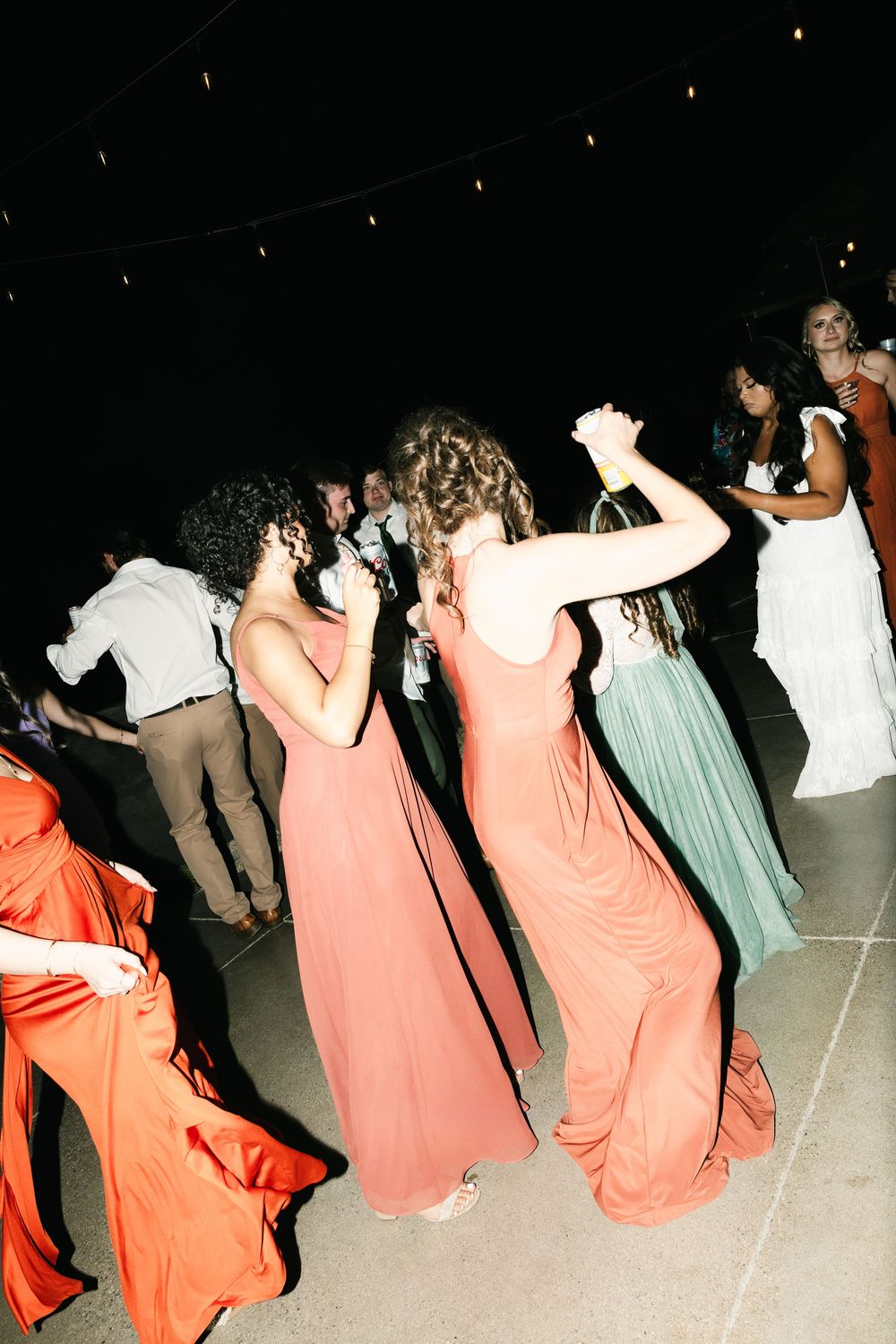 Wedding guests dance in a line wearing coral and mint colored dresses at a reception.