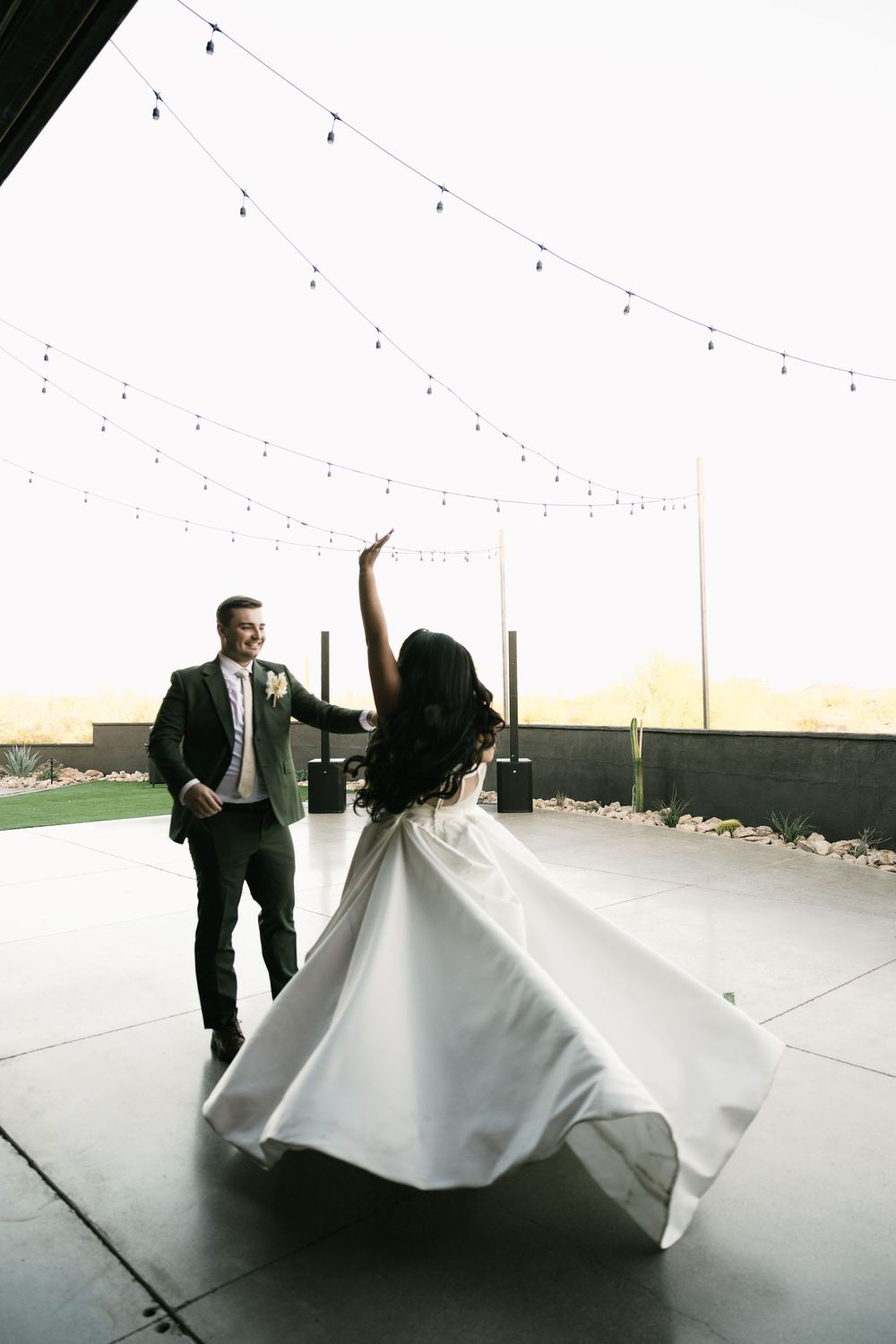 A couple dances with dramatic flair in a bright white reception space with string lights overhead.
