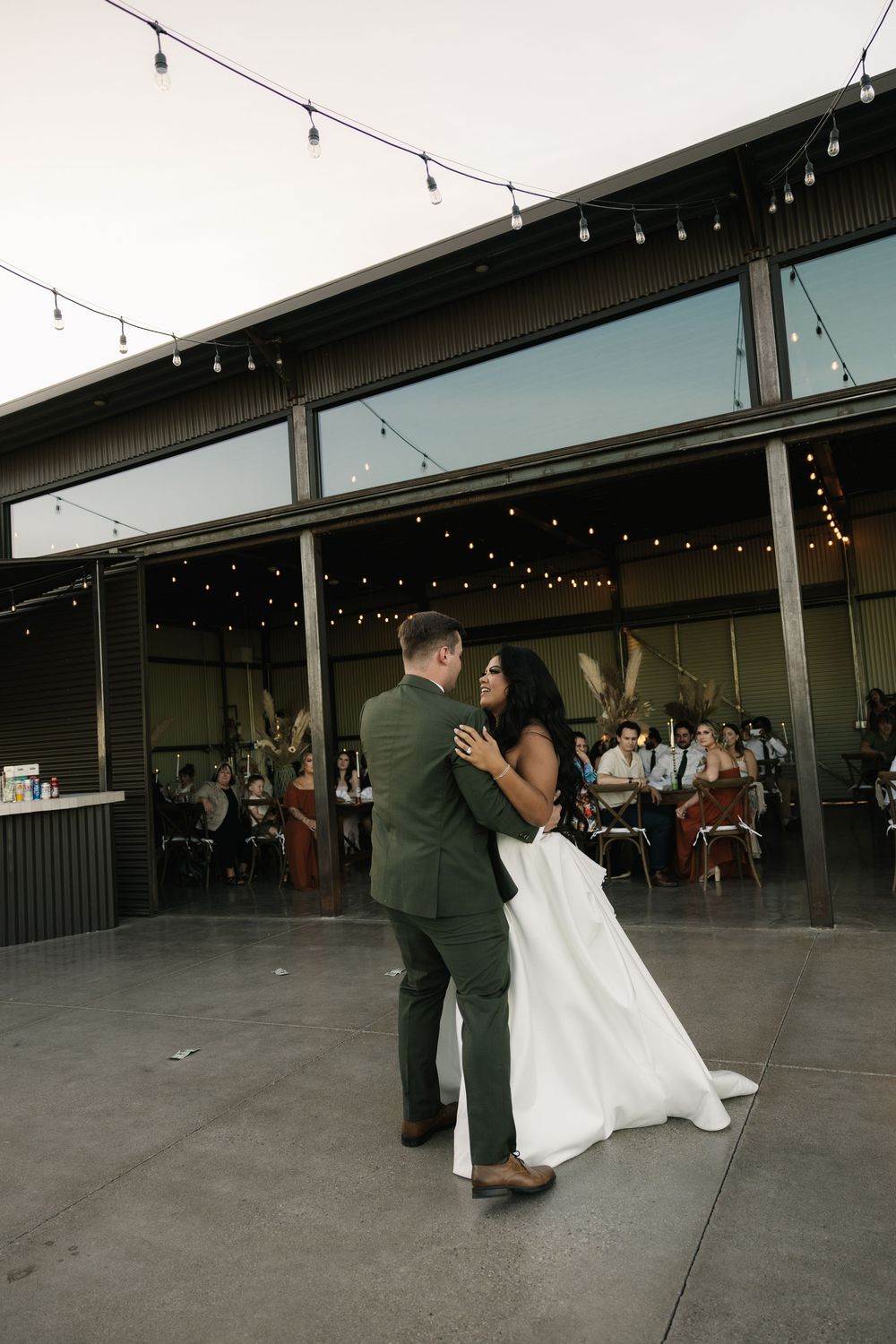 A couple shares a romantic dance moment under string lights at their wedding reception.