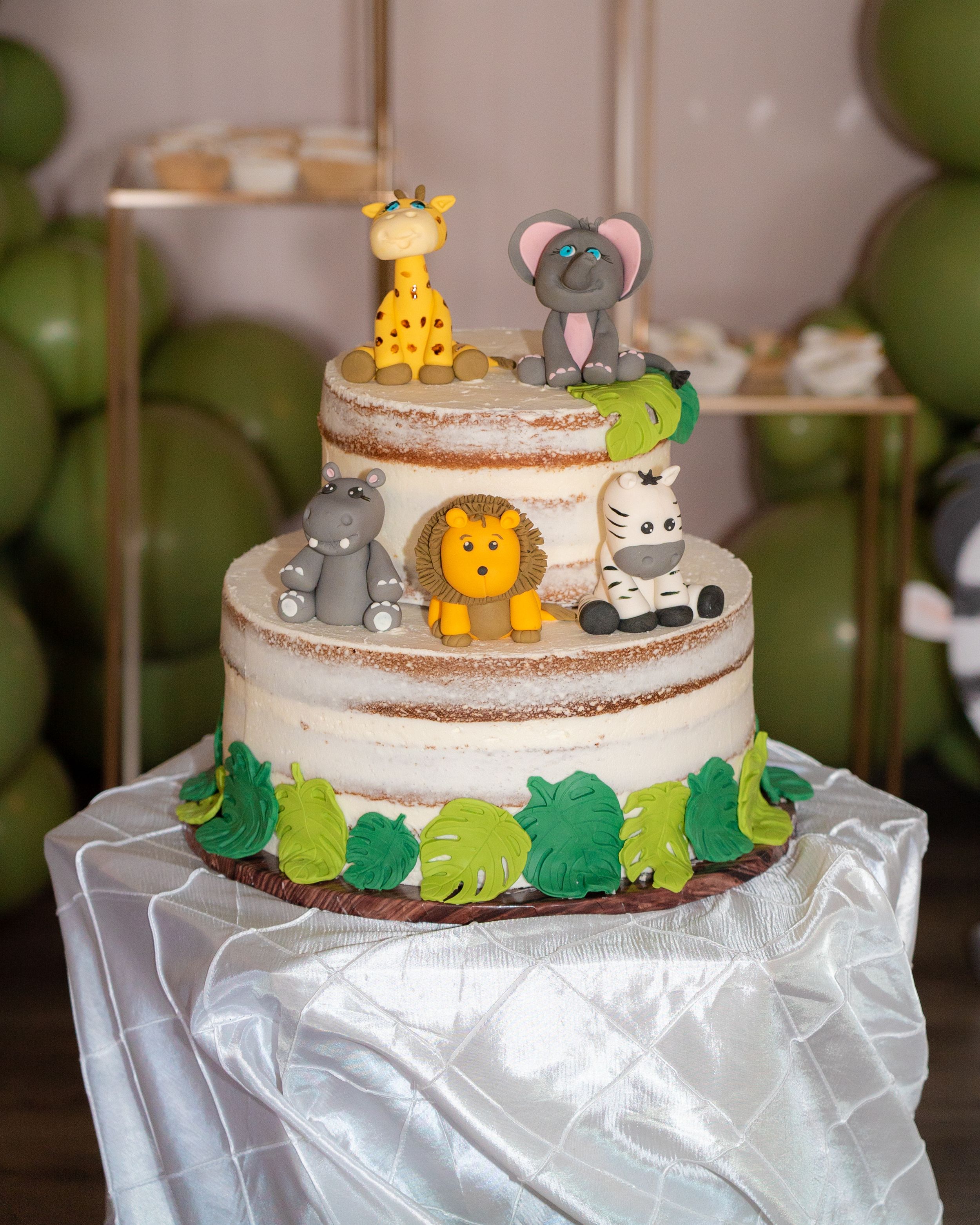 Two-tier safari themed cake with fondant animal toppers including giraffe, elephant, lion, hippo, and zebra.