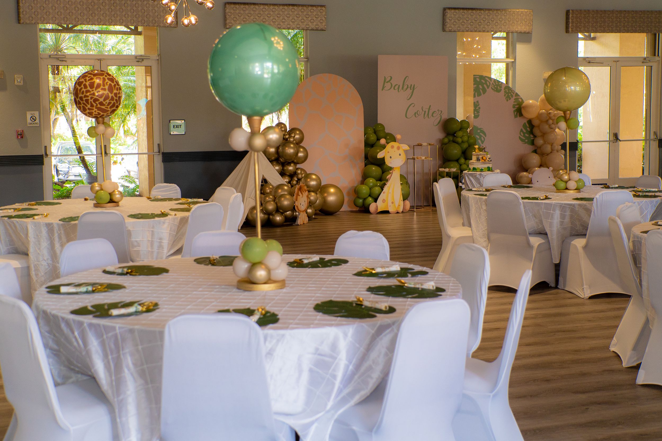 Elegant baby shower venue with white draped tables, gold accents, and large teal balloon centerpieces.