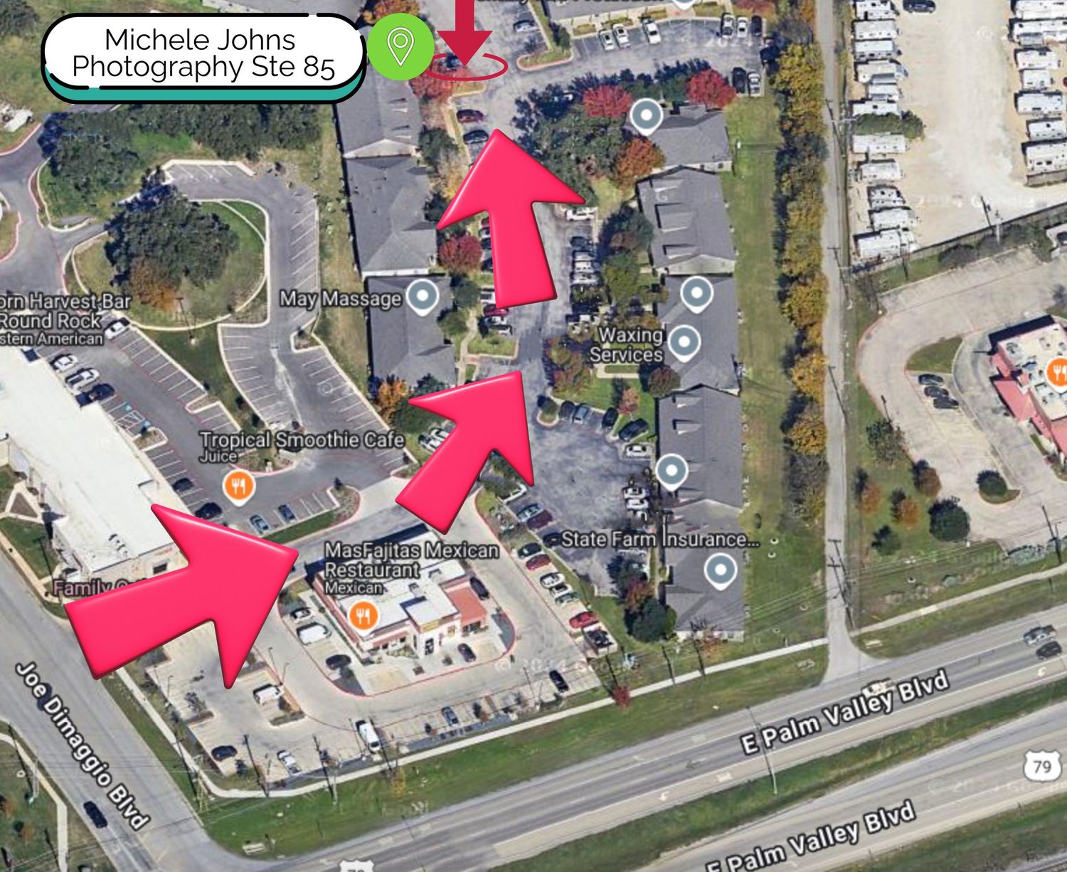 Aerial satellite view of a parking lot with red arrows pointing along a navigation path between buildings and roads.