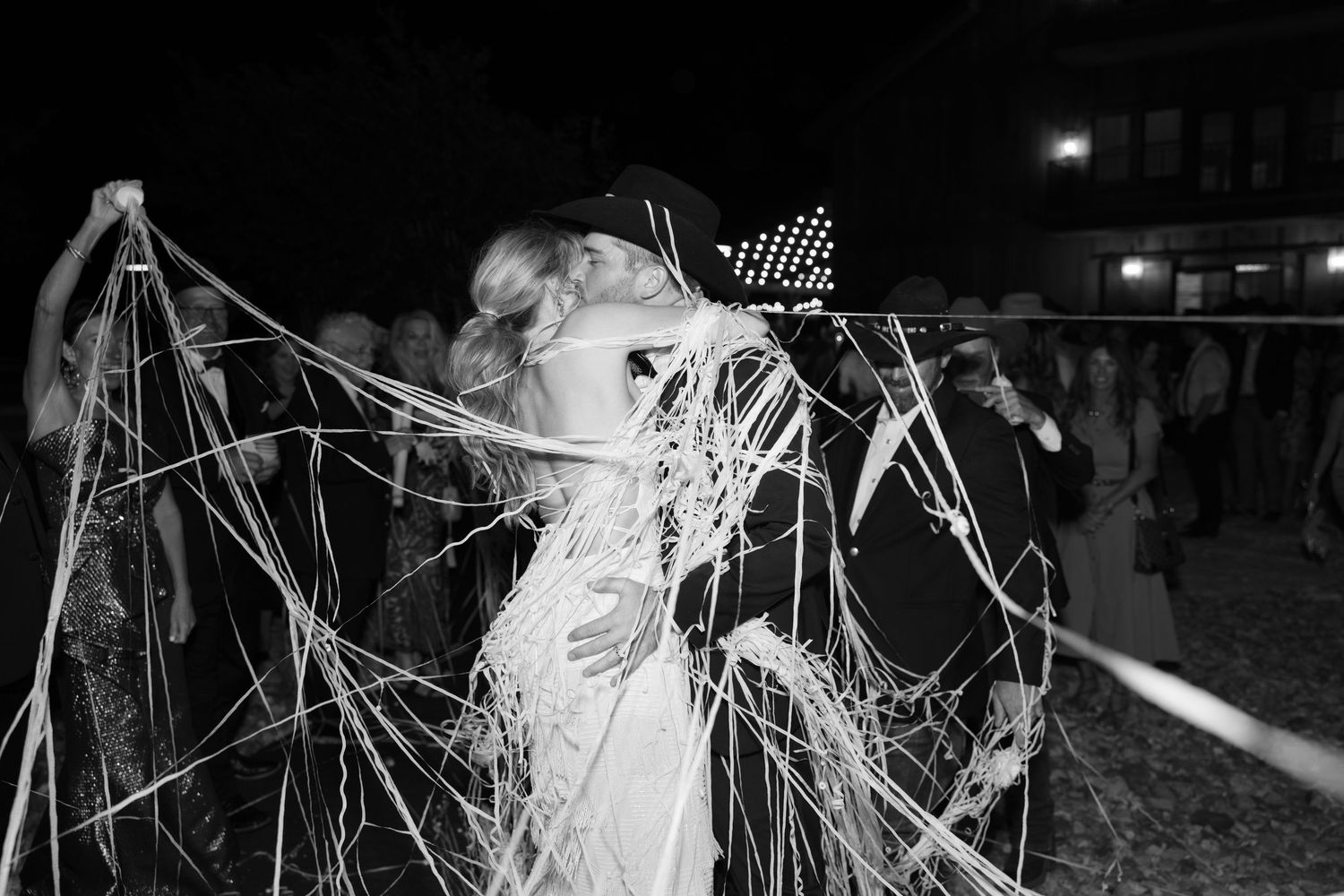 A group of silhouetted figures dance among illuminated sparklers and fireworks at an outdoor nighttime celebration.
