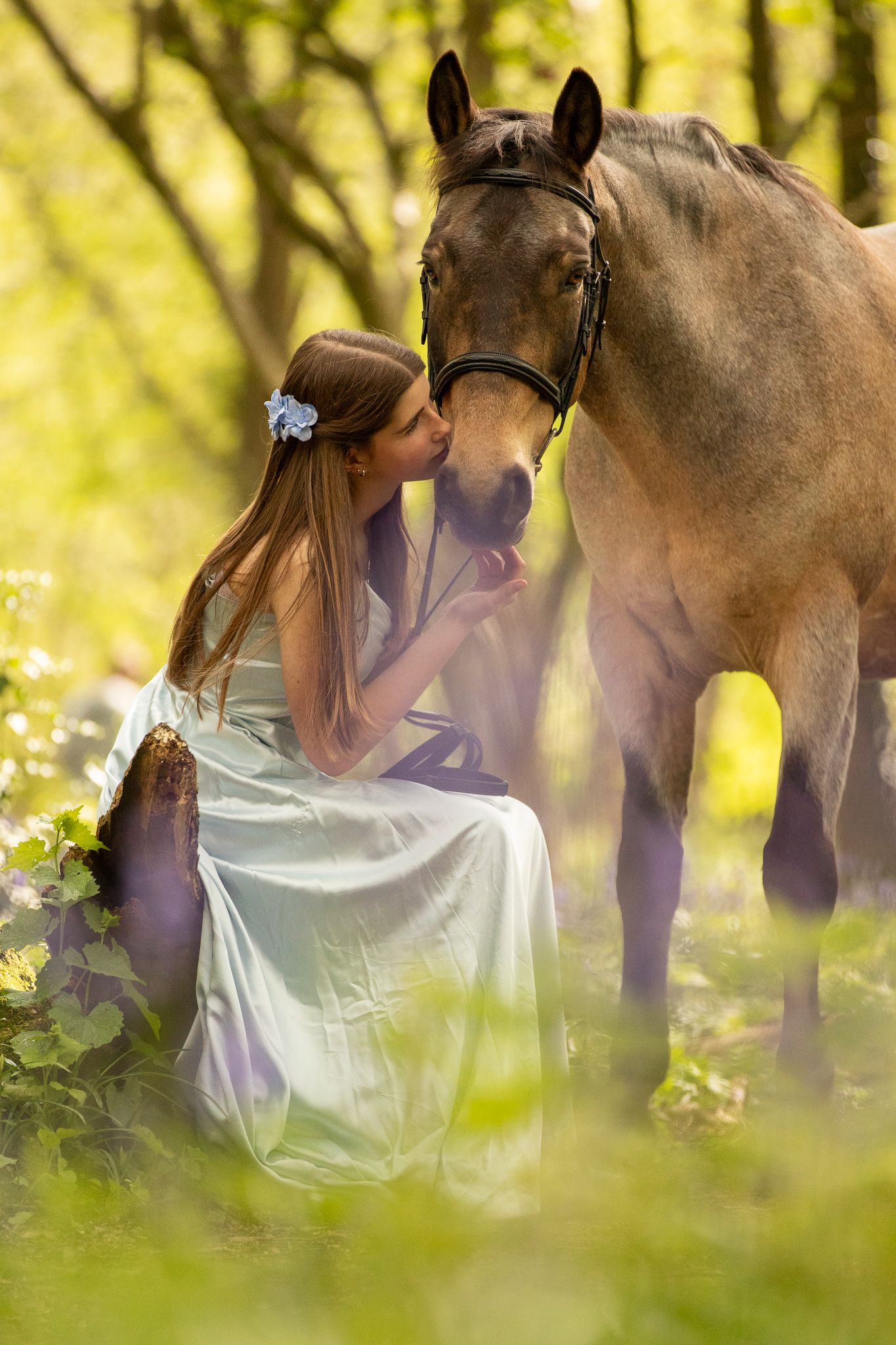 Young girl in denim overalls embraces a palomino horse in a sun-dappled forest setting.