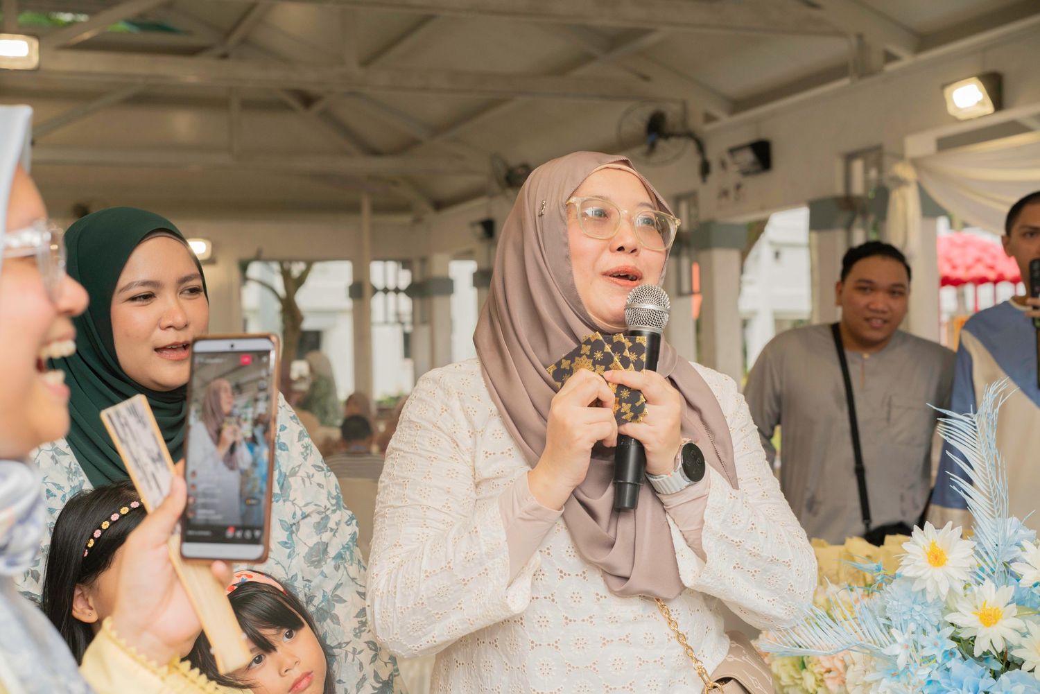 Wedding guests seated at a long table laugh and smile during a joyful outdoor celebration.