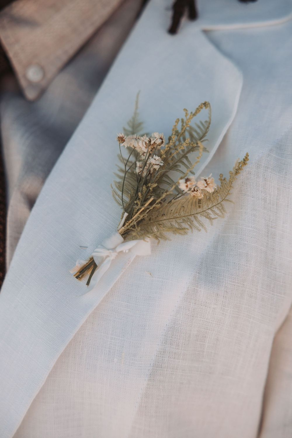 A series of delicate dried fern leaves decorated with gold paint arranged on white linen fabric in a minimalist style.