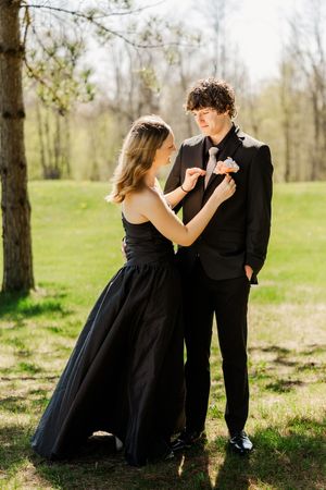 A couple in formal black attire shares a playful moment outdoors.