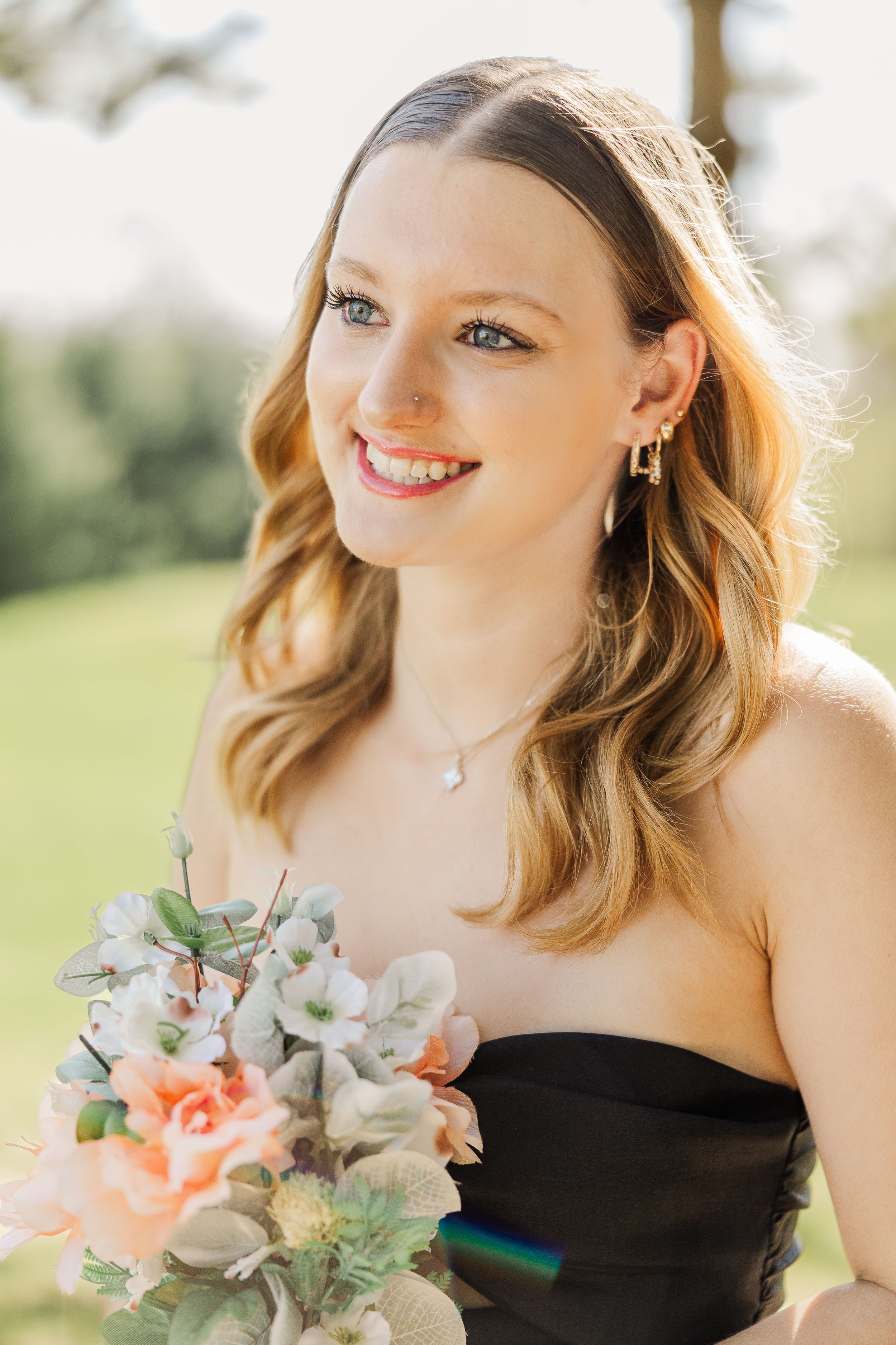 A person in a strapless black dress holds a delicate bouquet against a green background.