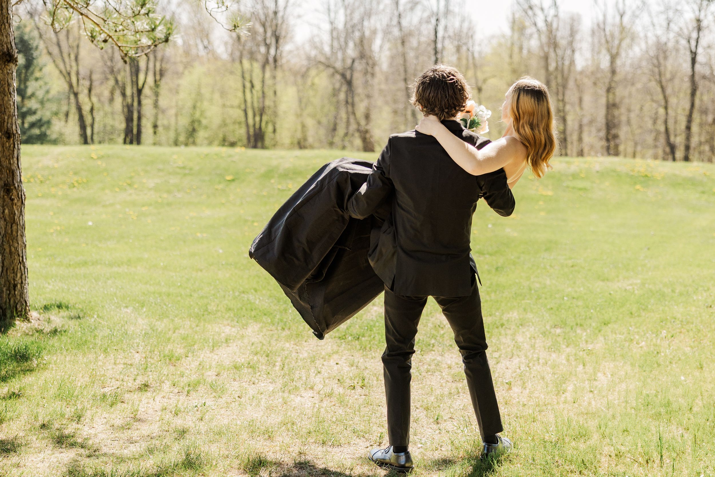 A couple in formal wear shares a playful moment in a spring garden setting.