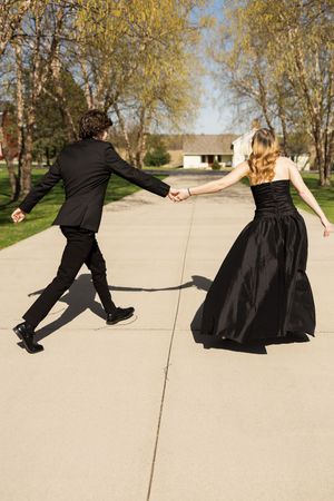 Couple in black formal wear playfully posing and dancing on a concrete path.