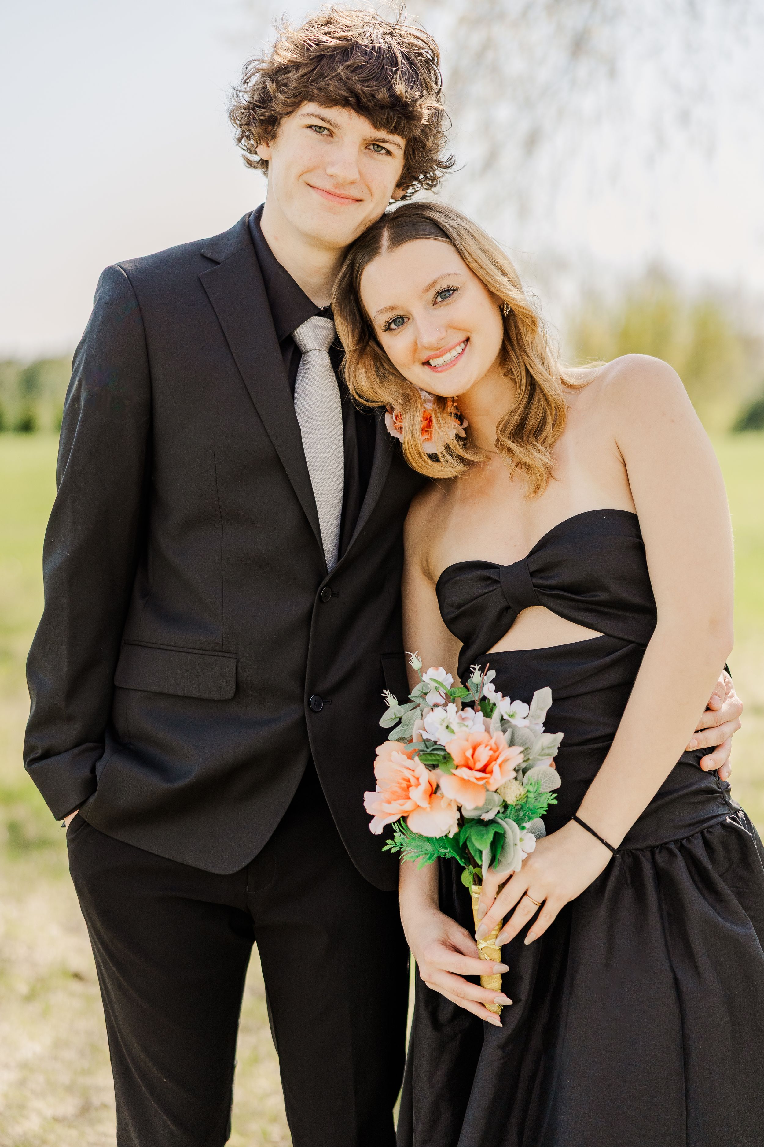 Couple in matching black formal wear pose with spring flowers for portraits outdoors.