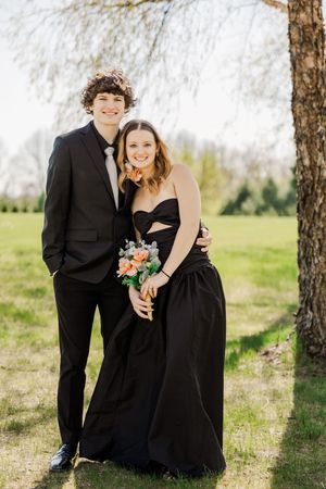 Formal couple poses together under willow trees holding spring bouquet.