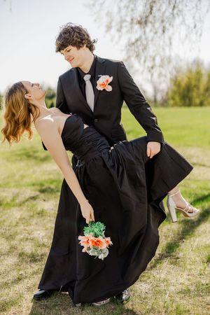Playful formal couple poses with flowers on grassy hill during spring photo session.