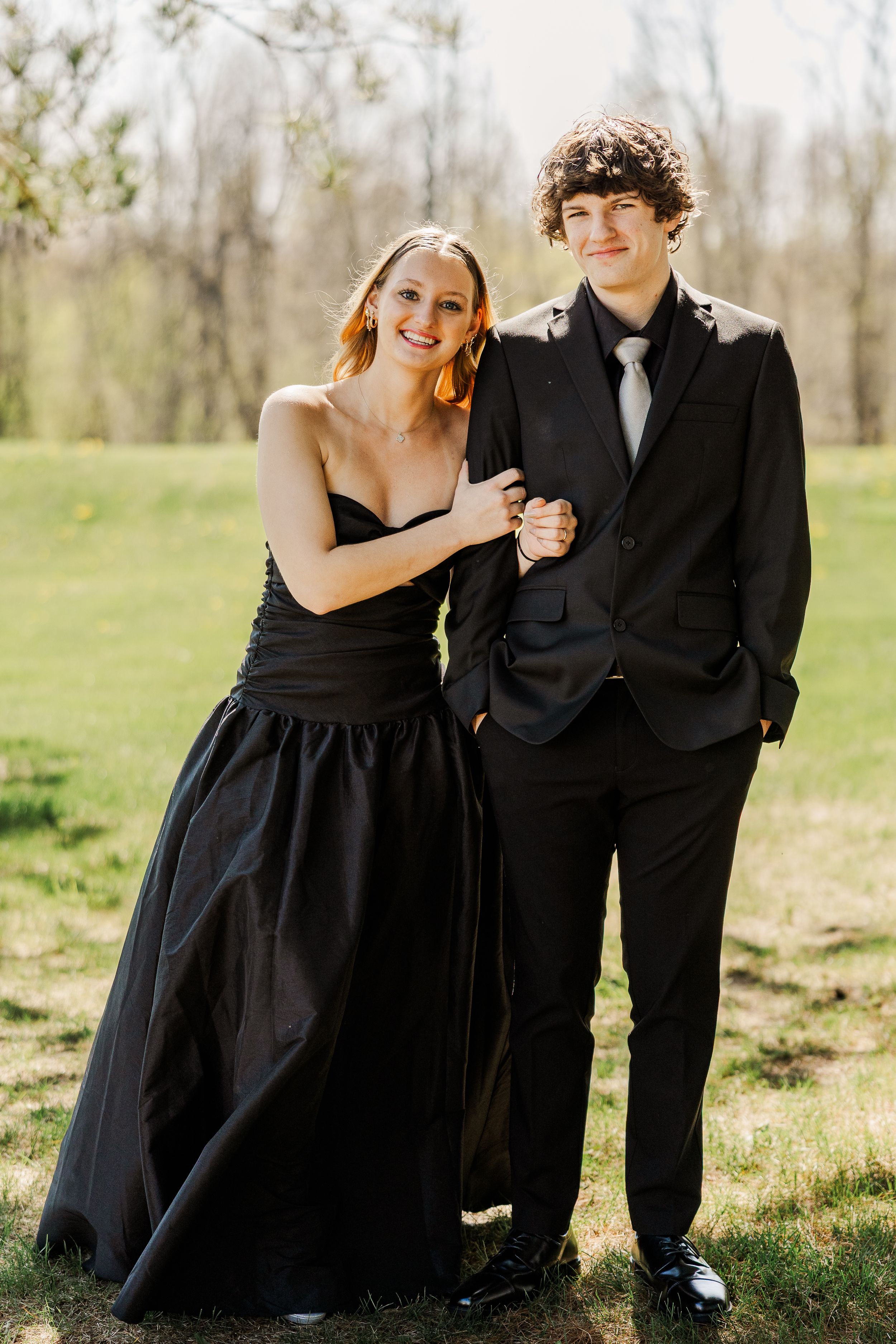 A couple in formal attire poses in a sunlit spring garden setting.